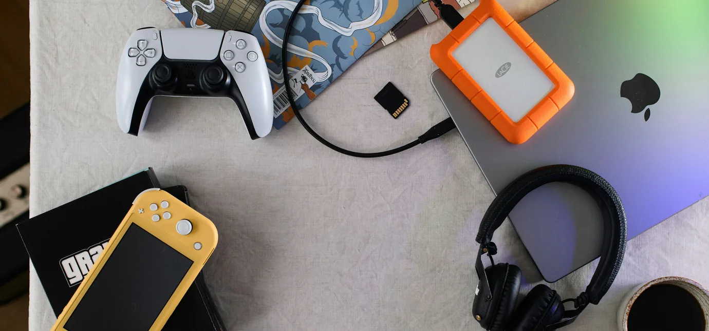 A game controller, handheld console, laptop, and headset arranged on one table